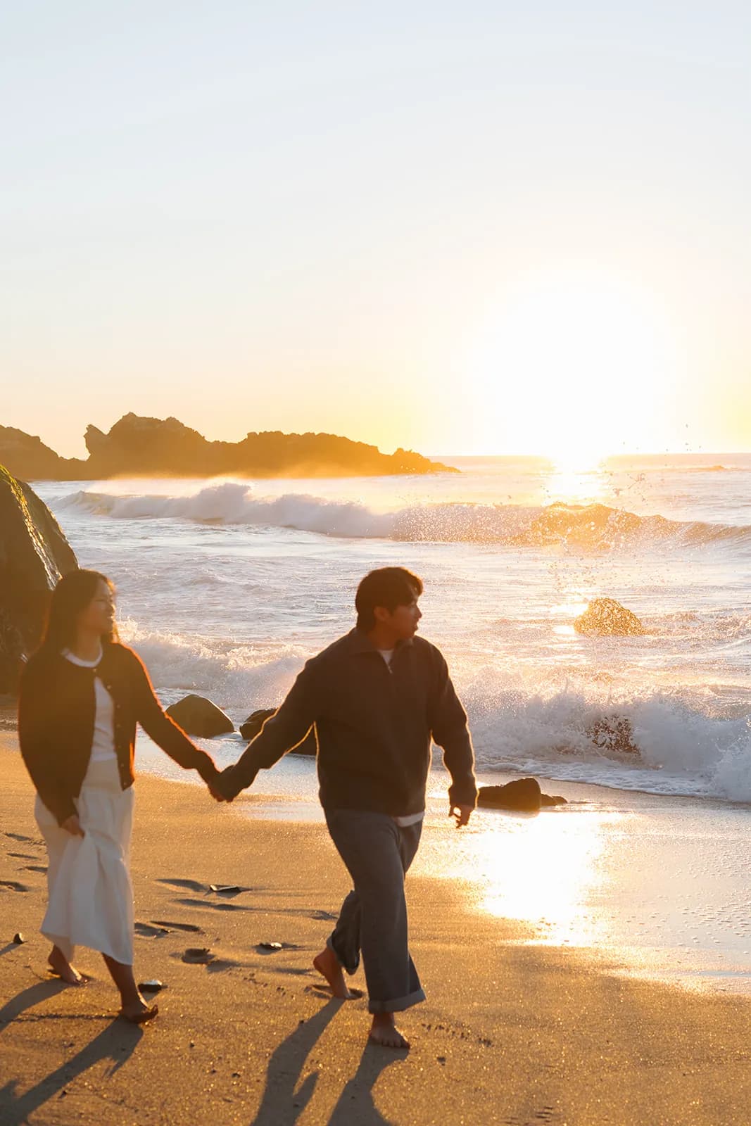 Angel and Mickey walking hand in hand along the shore at sunset