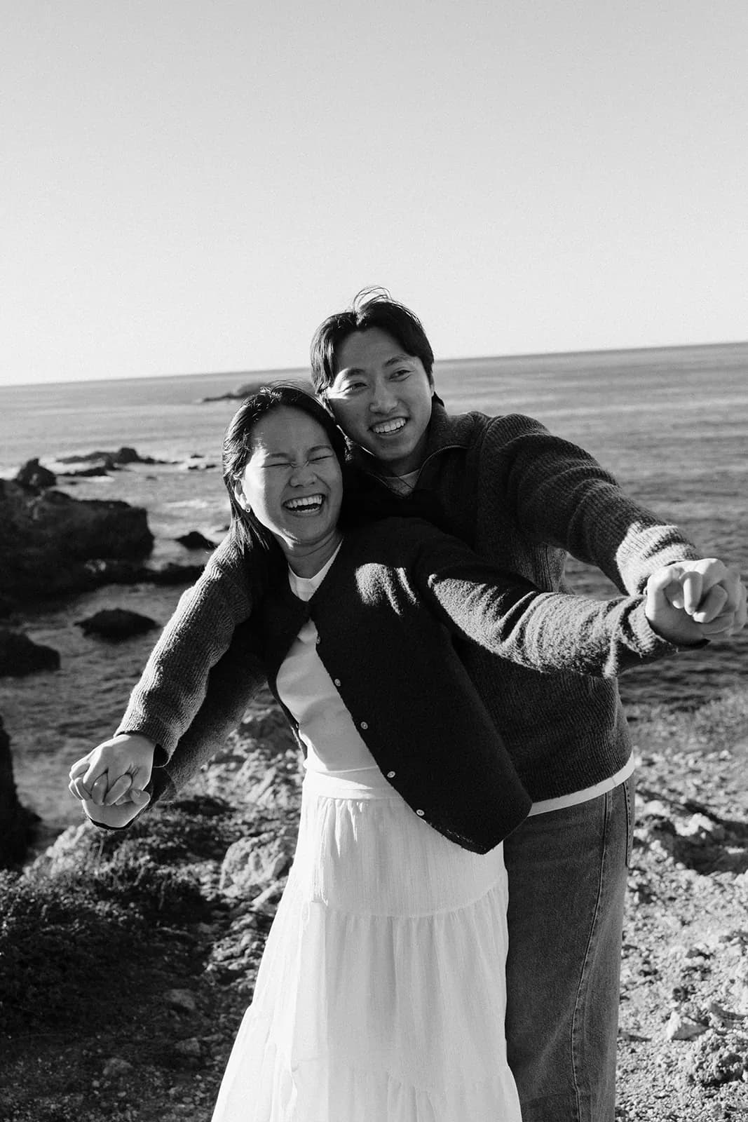 Angel and Mickey laughing together on a rocky shoreline